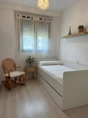 a white bedroom with a large bed and a chair at BAJO GUÍA DELUXE in Sanlúcar de Barrameda
