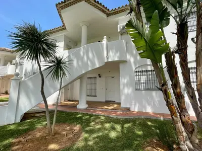 a white house with palm trees in front of it at Apartamento Columela in Chiclana de la Frontera