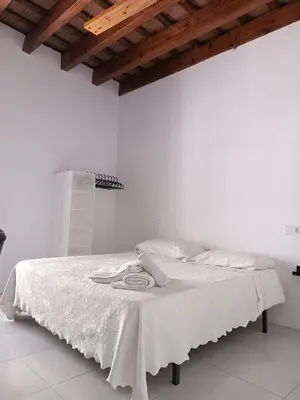 a white bed with white sheets and a wooden ceiling at Apartamentos Arquillo de Rota in Sanlúcar de Barrameda