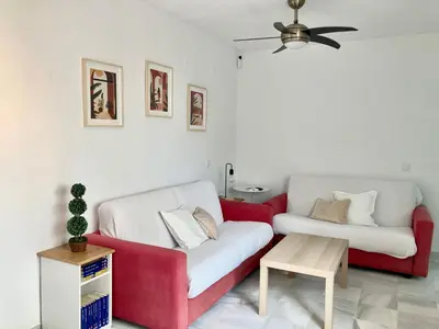 a living room with a red and white couch and a table at APARTAMENTO GENOVEVA PLAYA - Playa, Piscina, Wifi in El Puerto de Santa María