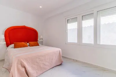 a bedroom with a bed with a red headboard and two windows at Casita de la coquina in Chiclana de la Frontera