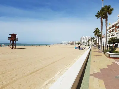a sandy beach with palm trees and a building at MyChoice Carmen in Rota