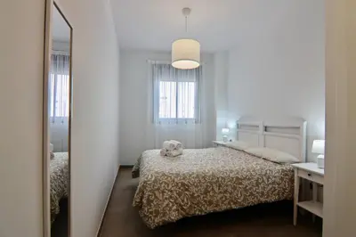 a white bedroom with a bed and a mirror at Apartamento San Leonardo Playa (Free Parking) in Cádiz