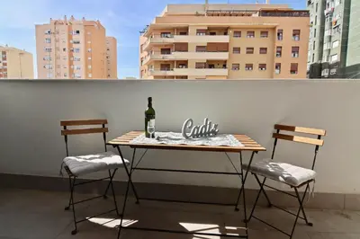 a table with a bottle of wine and two chairs on a balcony at Apartamento San Leonardo Playa (Free Parking) in Cádiz