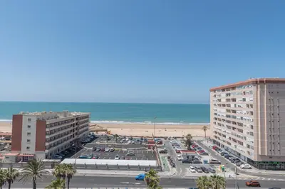 a parking lot next to a beach with two buildings at Apartamento Cortadura Playa in Cádiz