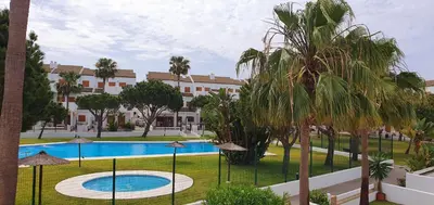 a resort with a pool and palm trees and a building at Appartement à 850 m de la plage de la Barrosa in Chiclana de la Frontera