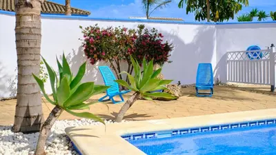 a swimming pool with two blue chairs and flowers at Villa Bananera Conil de la Frontera by Ruralidays in Conil de la Frontera
