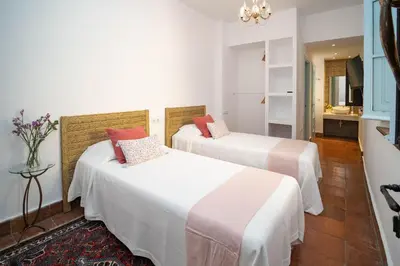 two beds in a room with white walls and red pillows at La Casa 1832 Boutique in Sanlúcar de Barrameda