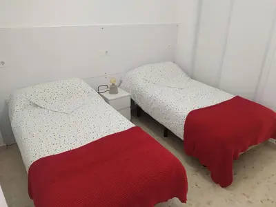two beds in a white room with a red blanket at Casa Julia in Sanlúcar de Barrameda