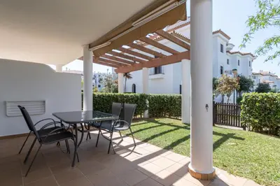a patio with a table and chairs under a pergola at Apartamento Planta Baja Coto Sancti Petri Playa de la Barrosa in Chiclana de la Frontera