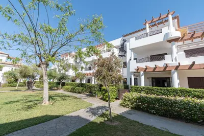 a large white building with a tree in front of it at Apartamento Planta Baja Coto Sancti Petri Playa de la Barrosa in Chiclana de la Frontera