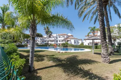 a swimming pool with palm trees and condos at Apartamento Planta Baja Coto Sancti Petri Playa de la Barrosa in Chiclana de la Frontera