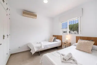 two beds in a white room with two windows at Villa Empul La Caracola in Chiclana de la Frontera