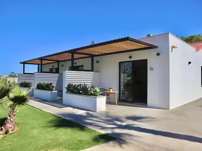 a white house with a wooden roof and some plants at Alojamiento rural FINCA AZUCENA SUITE only adults in Conil de la Frontera