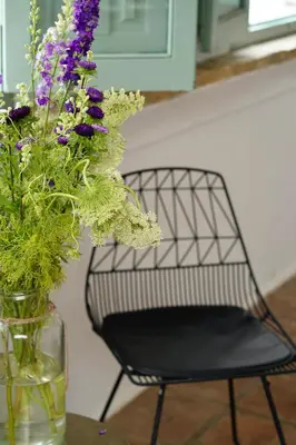 a glass vase with purple flowers and a chair at Alojamiento rural CASAPIÑA in Conil de la Frontera