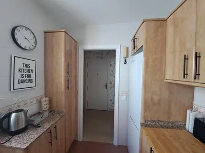a kitchen with wooden cabinets and a clock on the wall at Ático primera línea de playa con vistas al Mar-Climatizado-Wifi-Parking-Solo familias in El Puerto de Santa María
