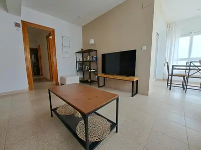 a living room with a flat screen tv and a table at Ático primera línea de playa con vistas al Mar-Climatizado-Wifi-Parking-Solo familias in El Puerto de Santa María