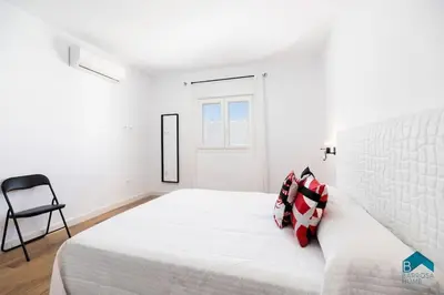 a white bedroom with a bed and a chair at Bisonte A in Chiclana de la Frontera