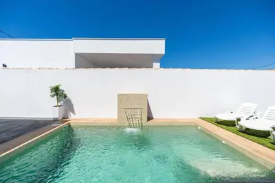 a swimming pool in front of a white building with chairs at Bisonte A in Chiclana de la Frontera