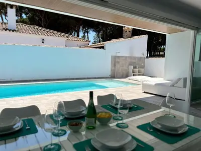 a dining table with a bottle of wine next to a swimming pool at Casa El Azul in Chiclana de la Frontera