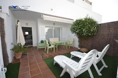 a patio with white chairs and a table at Adosado Familiar con Piscina y Terraza in Cádiz