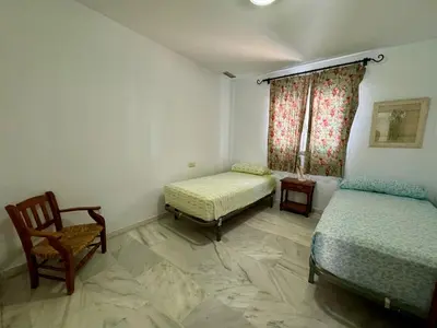 a room with two beds and a chair and a window at Hoyo 27 con Piscina Grupo AC Gestión in Chiclana de la Frontera