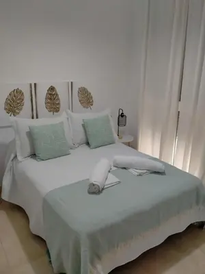 a white bedroom with a white bed with green pillows at Apartamento las tres lunas in Sanlúcar de Barrameda