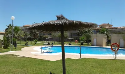 a large straw umbrella in front of a swimming pool at RESIDENCIAL EN BAJO DE GUIA in Sanlúcar de Barrameda