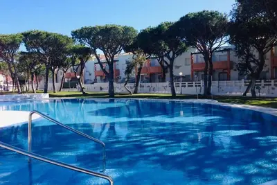 a large blue swimming pool with trees in the background at Apartamento con porche y piscina in Chiclana de la Frontera