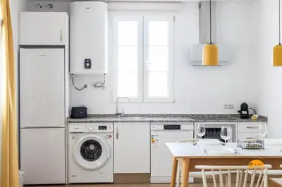 a white kitchen with a washing machine and a table at Mar de la Viña - Free Parking by Cádiz Time in Cádiz