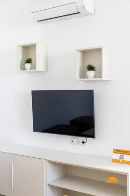 a flat screen tv on a white wall with two plants at Mar de la Viña - Free Parking by Cádiz Time in Cádiz