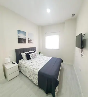 a white bedroom with a bed and a television at Apartamento Plaza Calzada 3 in Sanlúcar de Barrameda