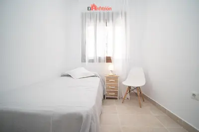 a white bedroom with a bed and a chair at Banda Playa - Arizón in Sanlúcar de Barrameda