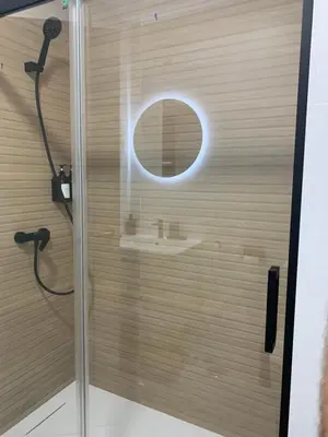 a shower with a glass door with a round mirror at Apartamento Al Andalus. La Barrosa. in Chiclana de la Frontera