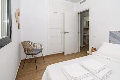 a white bedroom with a chair and a bed at Nautilus 3 - Elegante Apartamento para 6 con Piscina, Wifi y AC en Rota in Rota