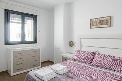 a white bedroom with a bed and a window at Nautilus 3 - Elegante Apartamento para 6 con Piscina, Wifi y AC en Rota in Rota