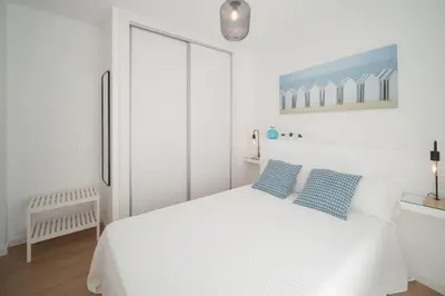 a white bedroom with a white bed with two blue pillows at Ático con terraza La Venencia in Sanlúcar de Barrameda