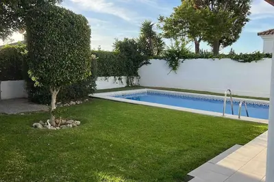 a swimming pool in a yard next to a white wall at APOLO in Chiclana de la Frontera