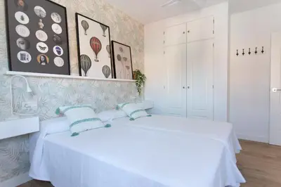 a white bedroom with a white bed with blue pillows at Aires de Doñana. Piscina y Playa. Parking gratis. in Sanlúcar de Barrameda