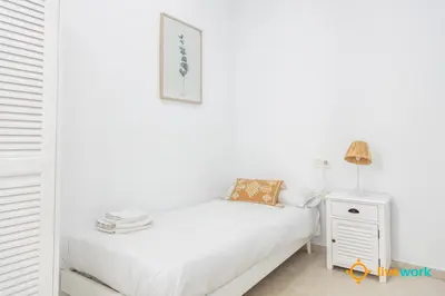 a white bedroom with a bed and a night stand at Apartamento Bike by LiveWork in Cádiz