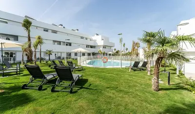 a group of chairs sitting in the grass near a pool at ÁTICOS ROTA Punta Candor in Rota