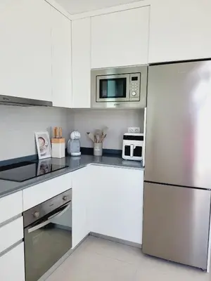 a kitchen with white cabinets and a stainless steel refrigerator at ÁTICOS ROTA Punta Candor in Rota