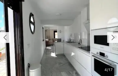 a white kitchen with a clock on the wall at Ático céntrico con terraza privada y plaza de garaje in Sanlúcar de Barrameda