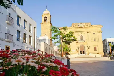 a building with a clock tower and flowers in front of it at Enjoy the historic center of Chiclana By C. Dreams in Chiclana de la Frontera