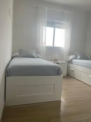 a white bedroom with two beds and a window at Anpartamento con Encanto Costa Ballena in Costa Ballena
