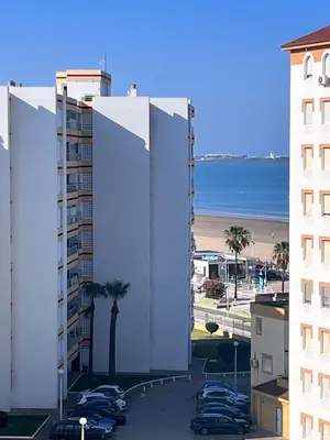 a white building with cars parked in a parking lot at Apartamento en primera línea de playa Valdemar 1 in El Puerto de Santa María