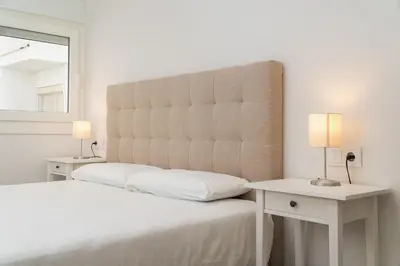 a white bedroom with a large headboard and two tables at Apartoyou - Enamorados in El Puerto de Santa María
