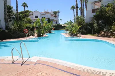 a large blue swimming pool with palm trees and buildings at Ático Costa Ballena playa infante. 1º línea playa in Rota