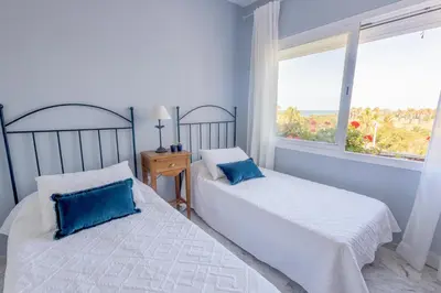 two beds in a room with a large window at Ático Costa Ballena playa infante. 1º línea playa in Rota