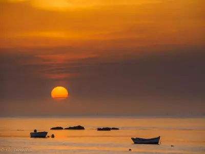 a sunset over the ocean with two boats in the water at apartamentos Larios centro in Sanlúcar de Barrameda